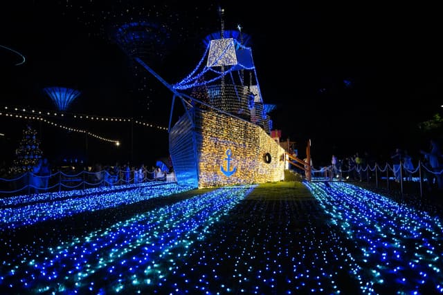 A nighttime scene of a lit-up creation resembling a ship, surrounded by blue LED lights strewn across the ground, giving the impression of a sea of lights