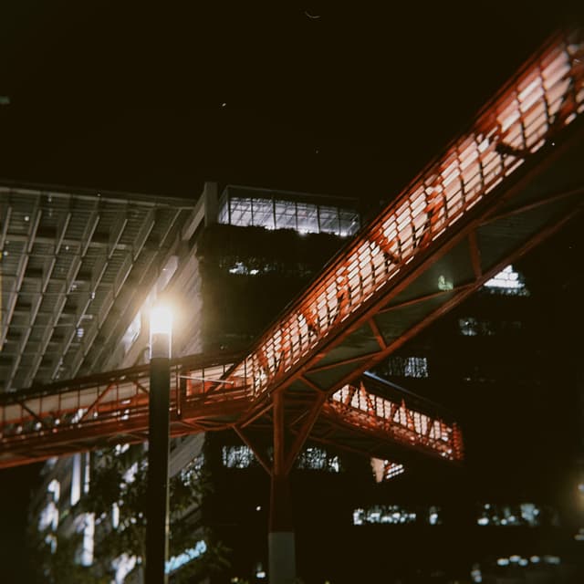 A red metal bridge illuminated at night with a streetlight and building lights visible