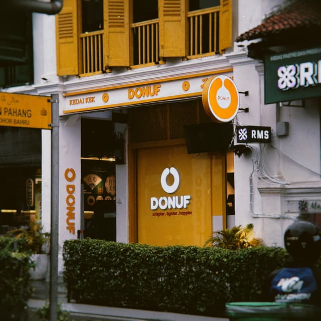 A storefront with a white and yellow facade featuring orange accents and a sign reading DONUF in white letters on a yellow door
