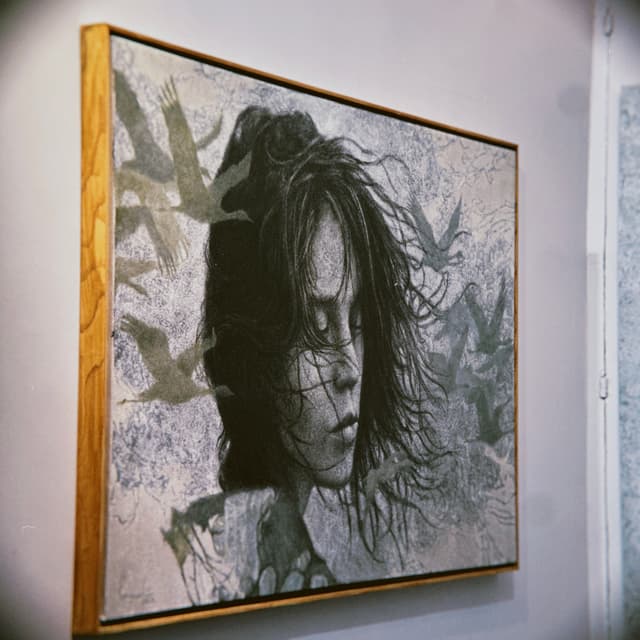 A framed portrait of a person with dark hair hangs on a wall, surrounded by a design of leaves and birds