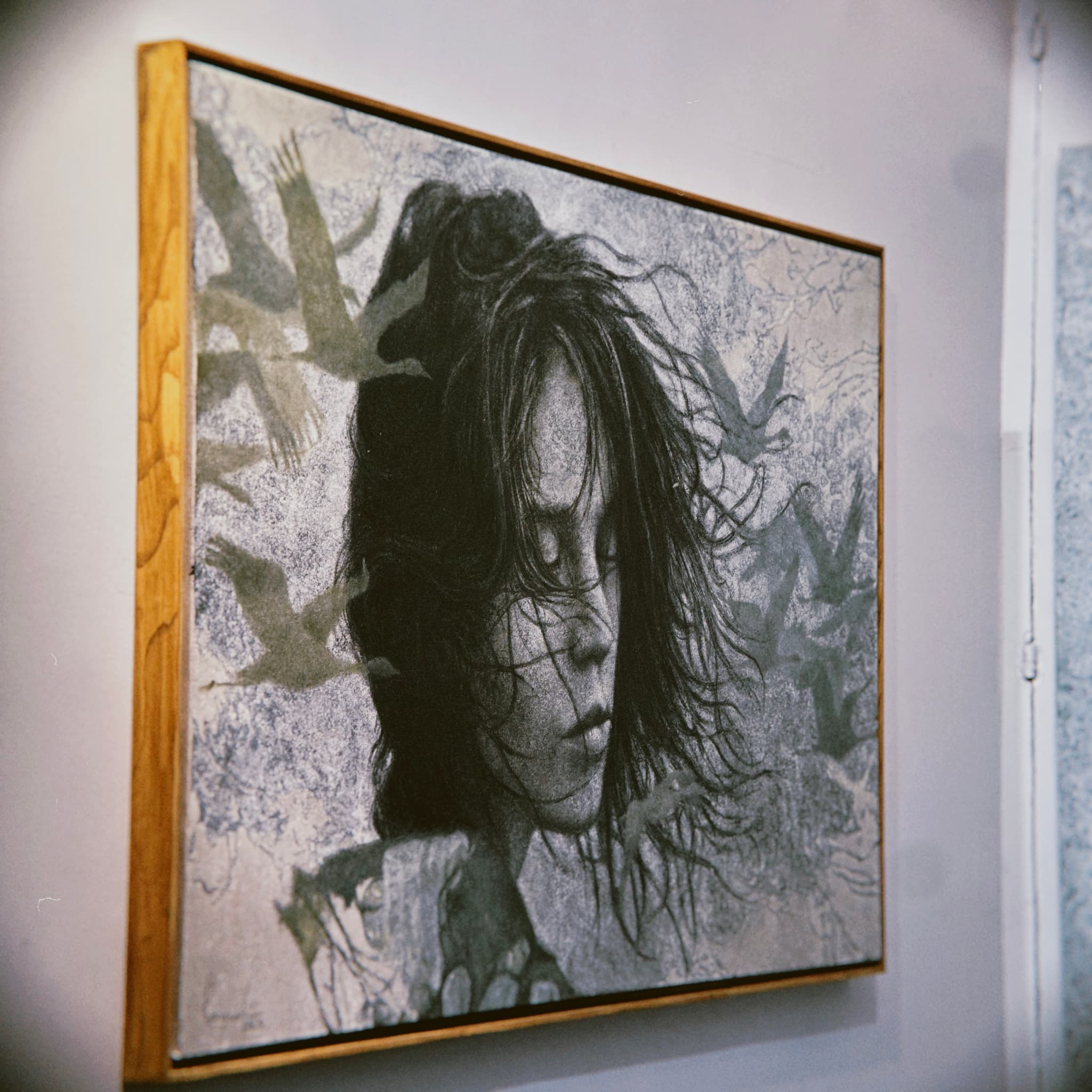 A framed portrait of a person with dark hair hangs on a wall, surrounded by a design of leaves and birds